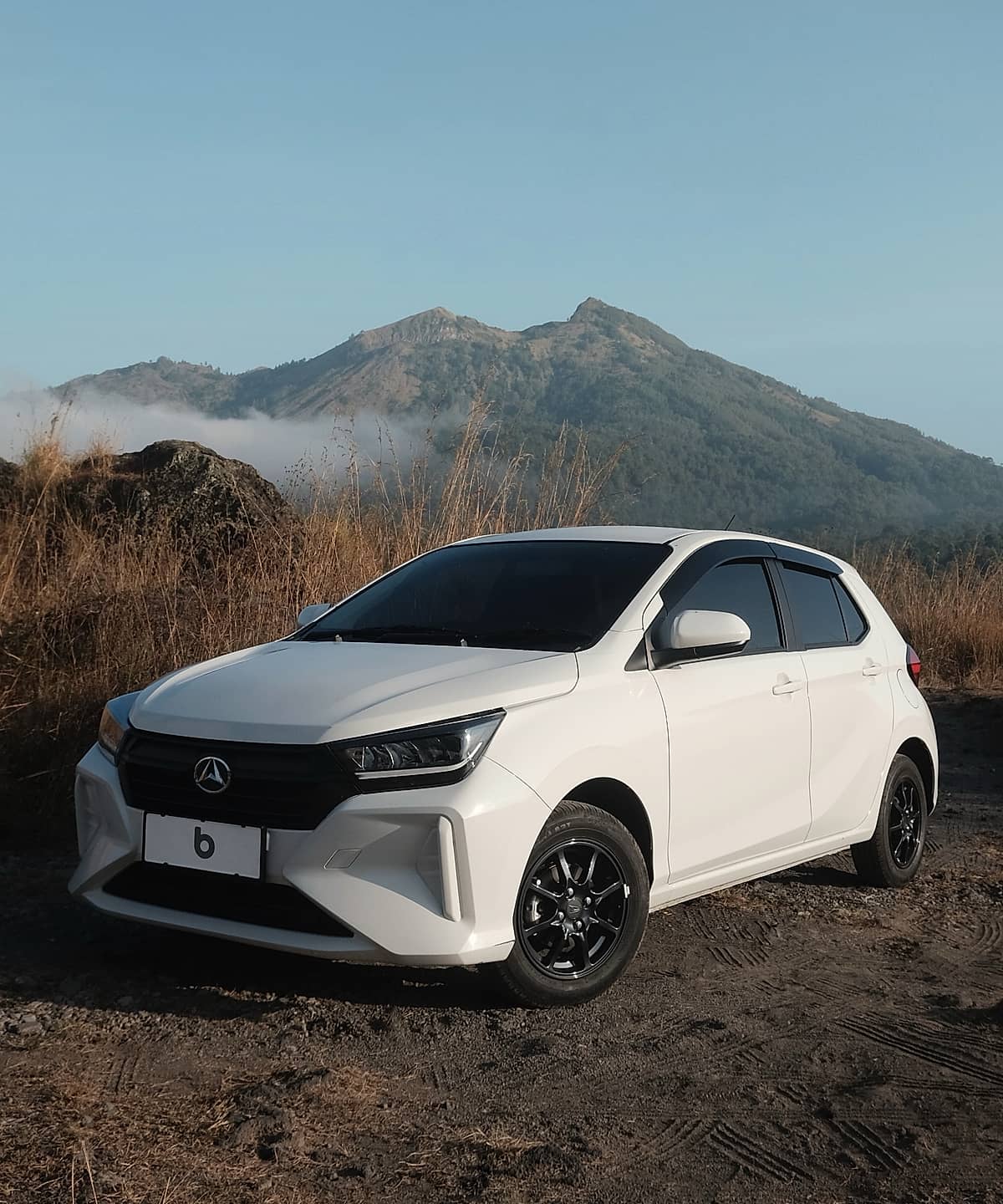 Car parked on a dirt road with a scenic mountain backdrop and dry grass fields.