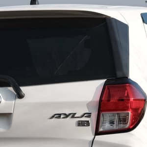 White Agya parked on a dirt road surrounded by tall dry grass and a misty sky.
