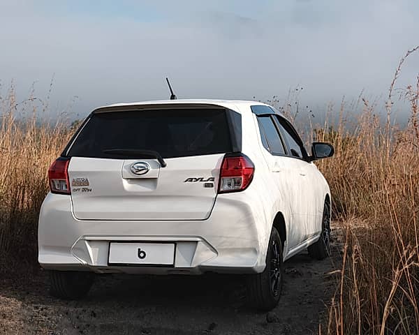 White Agya parked on a dirt road surrounded by tall dry grass and a misty sky.