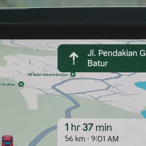 Close-up of a car's infotainment system with a navigation app guiding through Bali's landscape.
