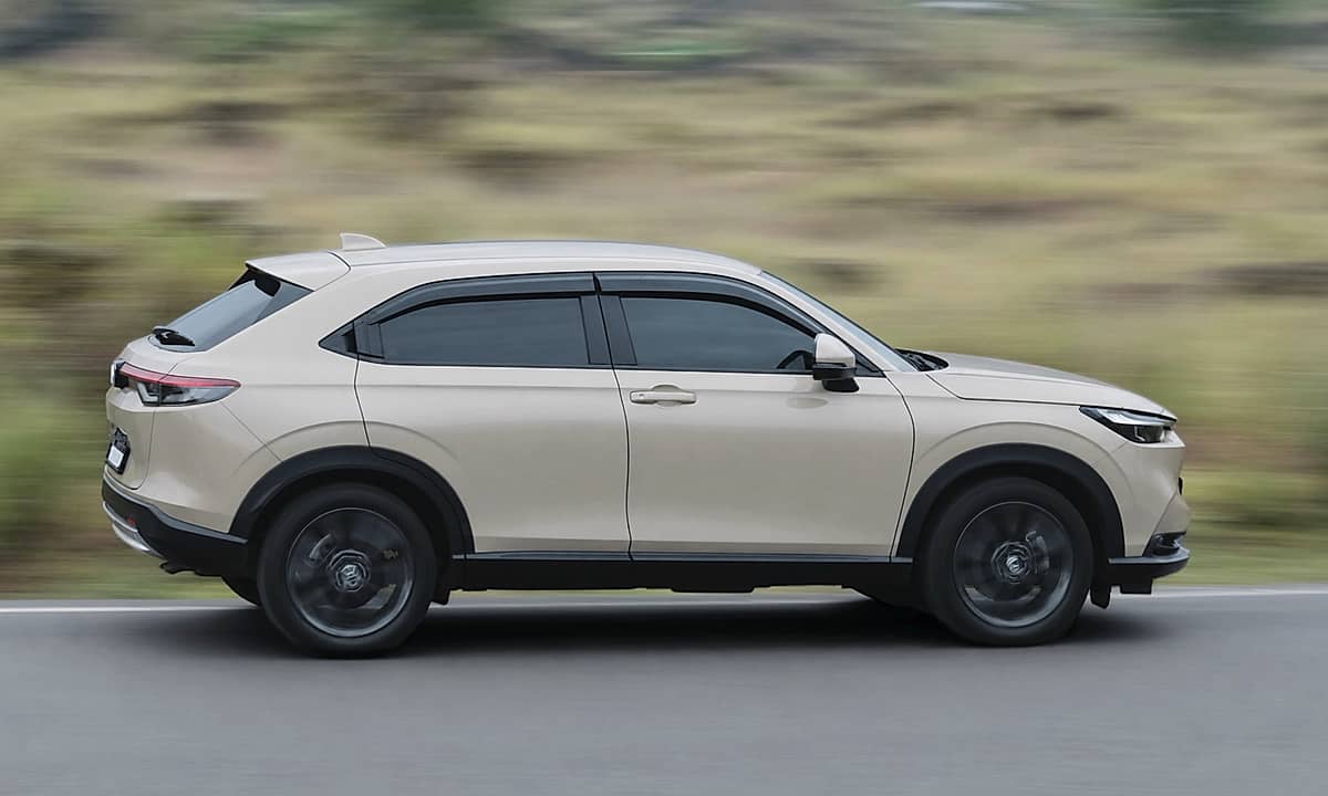 Light-colored Honda HRV crossover SUV in profile shot move quickly along a road.