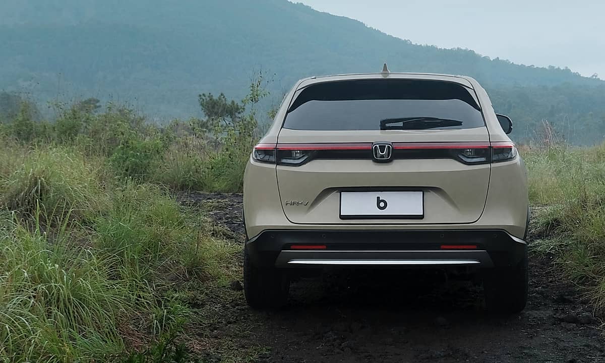 A beige Honda HRV parked on a dirt road with lush green grass and mountains in the background.