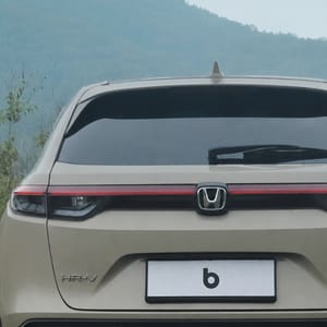 A beige Honda HRV parked on a dirt road with lush green grass and mountains in the background.