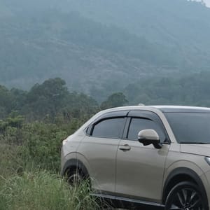 A silver Honda HR-V parked on a grassy slope with a misty mountain range in the background, suggesting adventure and scenic drives in Bali.