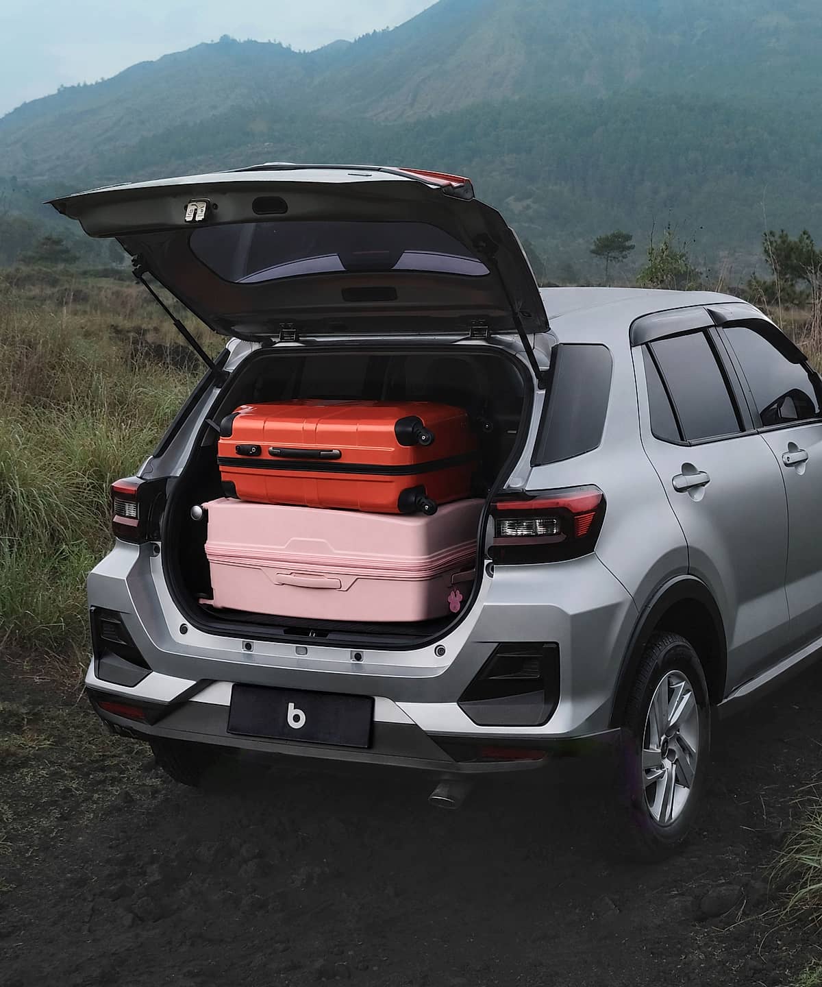 Rear view of Toyota Raize loaded with travel bags, positioned on a dirt road amidst lush green vegetation.