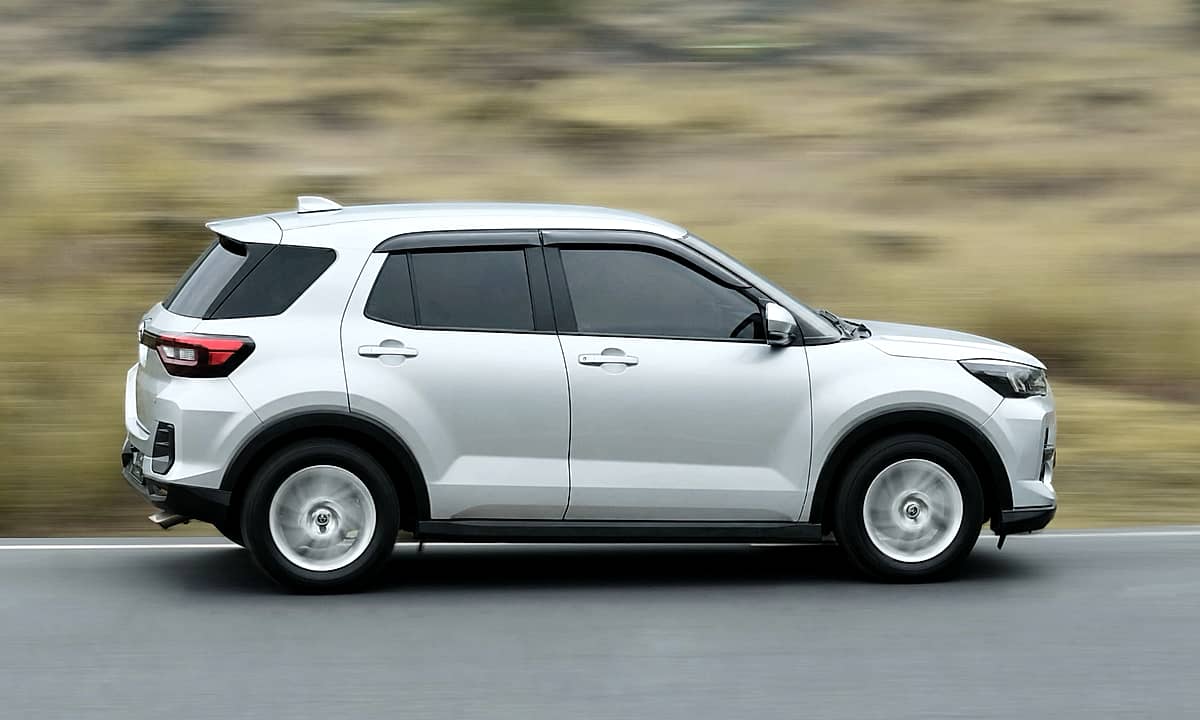 The side profile of a  silver Toyota Raize captured with a blurred natural landscape behind it.