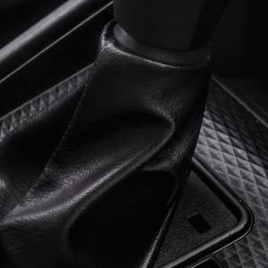 Close-up of an automatic gear shifter in a modern car interior, showcasing a textured black panel and a leather-wrapped shift knob with gear indicators.