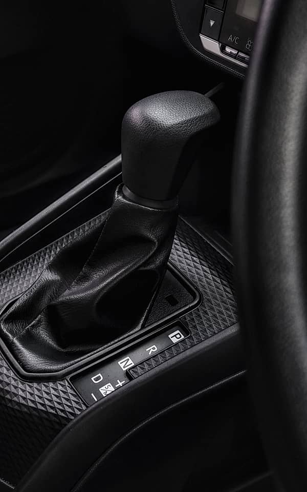 Close-up of an automatic gear shifter in a modern car interior, showcasing a textured black panel and a leather-wrapped shift knob with gear indicators.