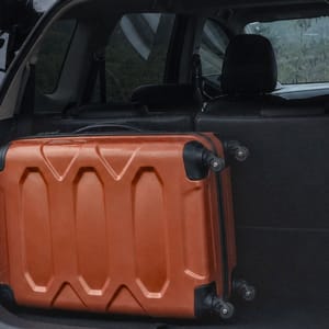 Black Mitsubishi Xpander with open trunk and orange suitcase in a rural Bali landscape.