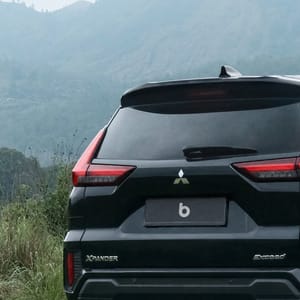 Black Mitsubishi Xpander parked on a dirt road in a rural Balinese landscape with rolling hills and lush vegetation.