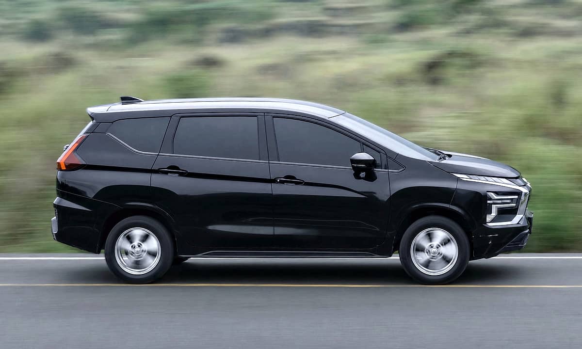 Black Mitsubishi Xpander MPV driving on a asphalt road with green, hilly background.