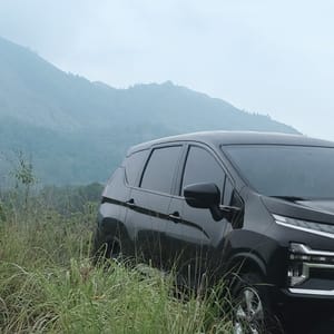 An adventurous shot of a black Mitsubishi Xpander positioned on a rough path, with a focus on the vehicle and the natural, overcast landscape of Bali.