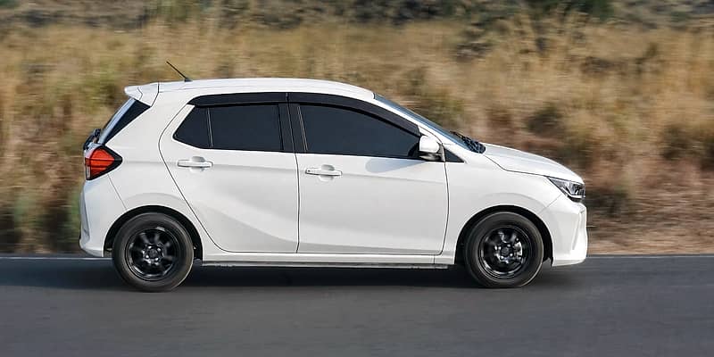 Dynamic shot of a white Toyota Agya  on a rural road in a Balinese setting.