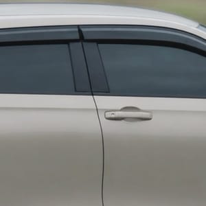 Side view of a light-colored Honda HR-V driving on a paved road with blurred green hills and trees in the background.