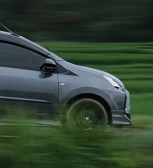 A dark gray hatchback drives past lush green rice paddies